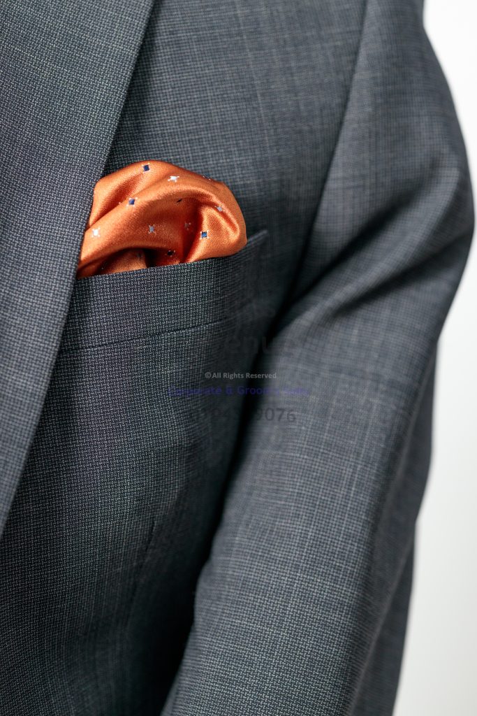 Close-up of a charcoal checked jacket lapel and an orange pocket square